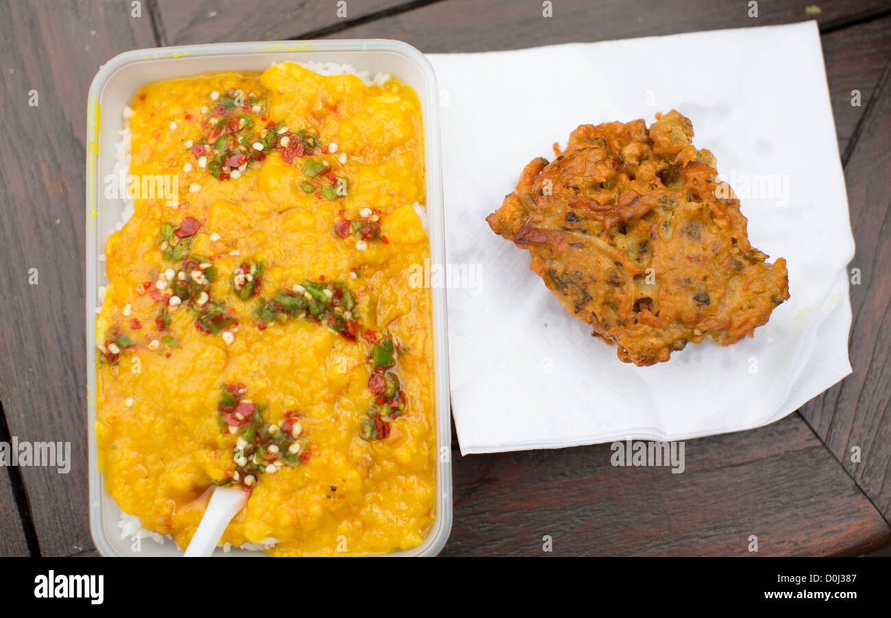 Fresh yellow lentil dal curry and onion bhaji in a takeaway container on a table outdoors Stock