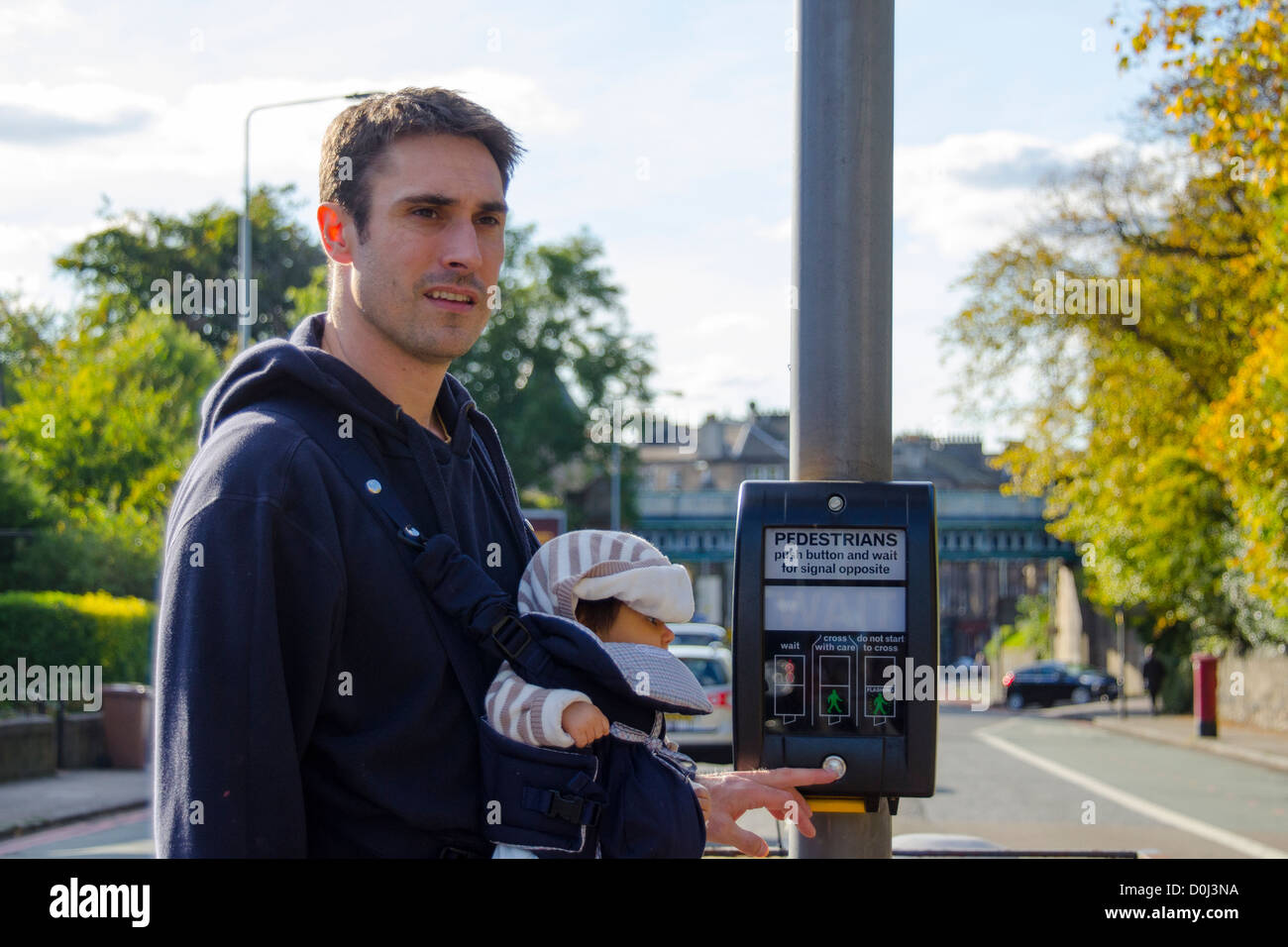Dad with baby in carrier crossing road using pedestrian crossing, Edinburgh, UK Stock Photo