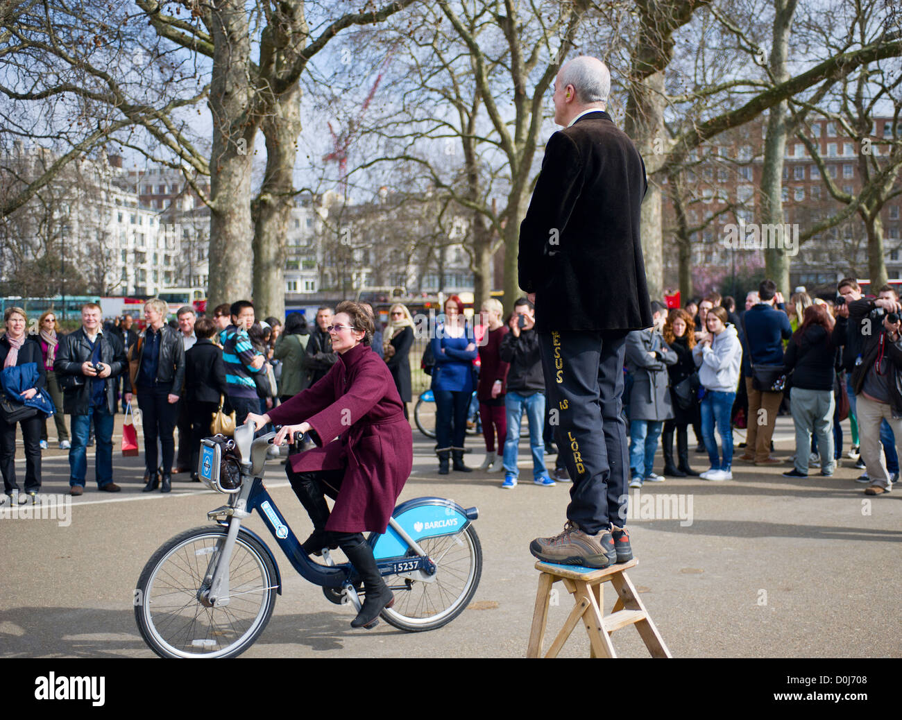A woman riding a bicycle past a man precahing at Speakers Corner in London. Stock Photo