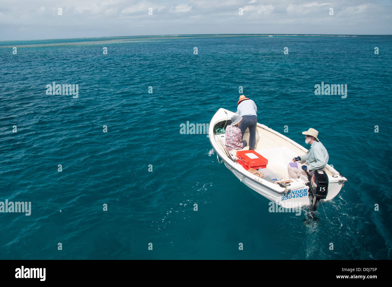 A small boat with three people heads out fishing on flat seas on Australia's Great Barrier Reef. Stock Photo