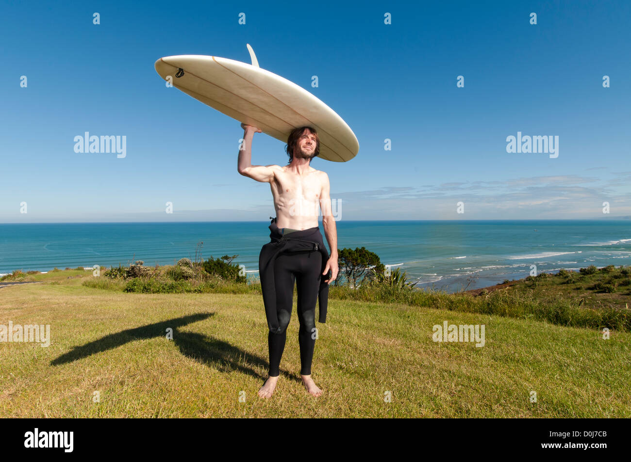 Male surfer standing with longboard on top of head with wetsuit down to his waist, Raglan New Zealand. Stock Photo