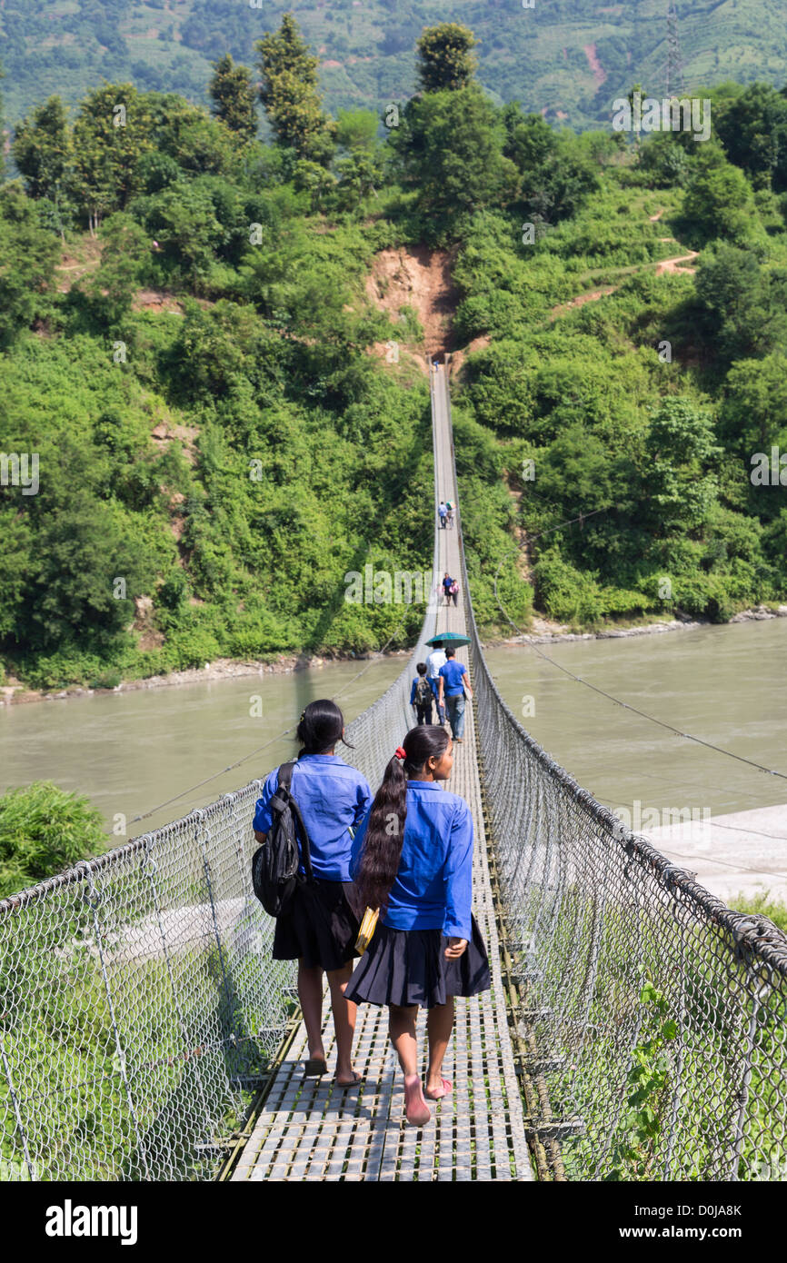 2 girls crossing a chain-bridge in Nepal on the road from Kathmandu to Pokhara Stock Photo