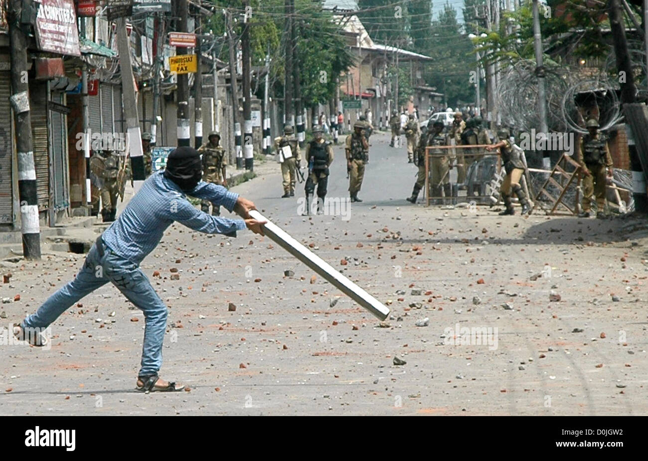 A masked Kashmiri protester tries to hit a stone thrown at him by paramilitary soldiers with a block of wood, during a protest Stock Photo