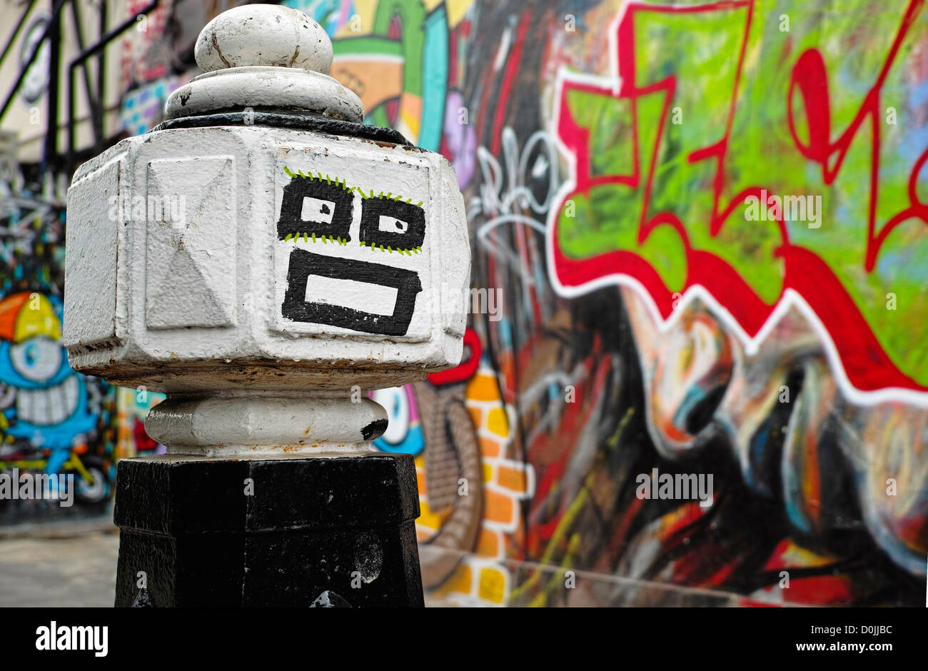 Brick Lane bollard face with graffiti behind. Stock Photo
