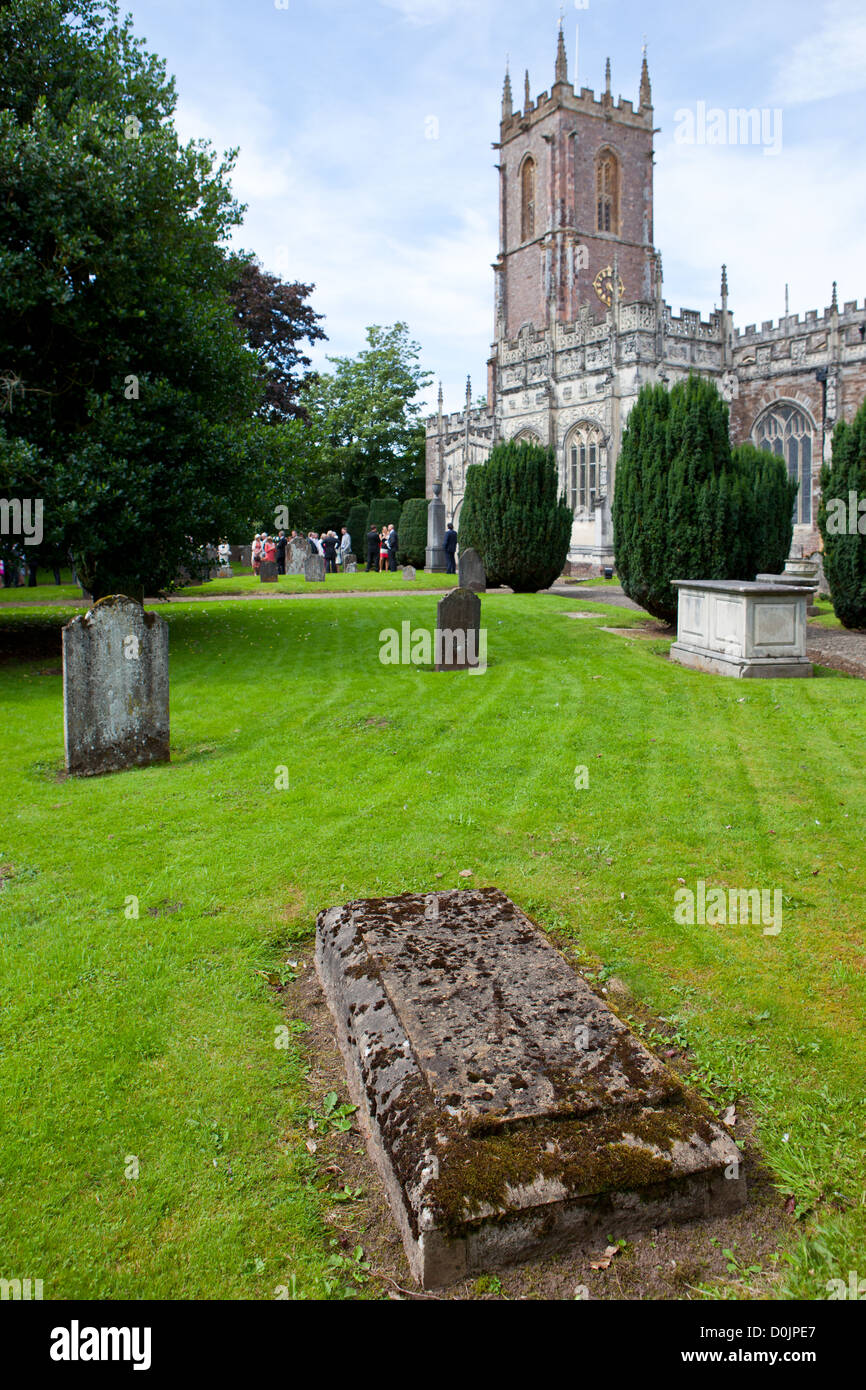 Tiverton, UK: One grave in the garden of Saint Peter's Parish Church. In the background, a wedding ceremony is held. Stock Photo