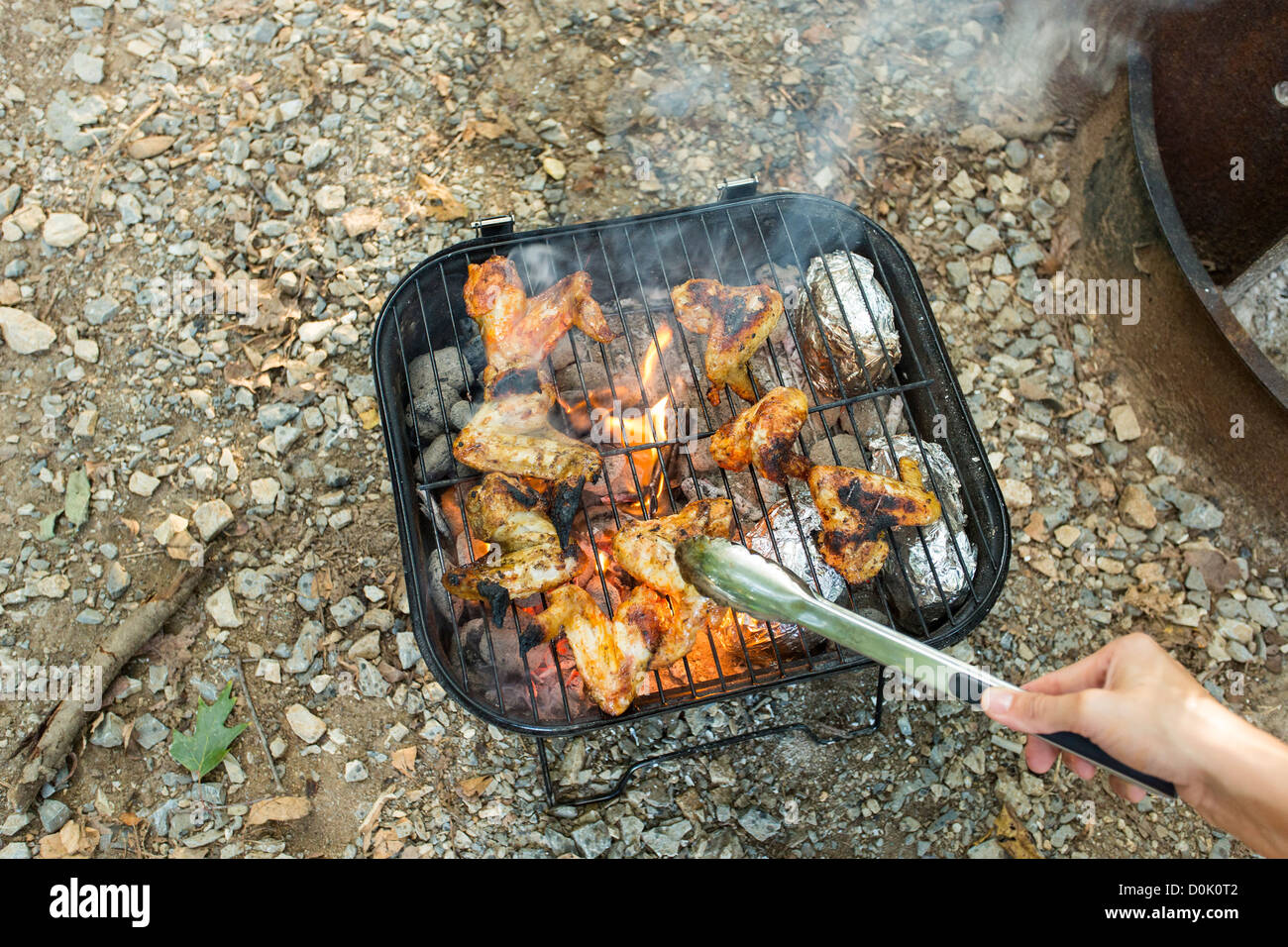 Hand holding grill tongs and turning a chicken wing over Stock Photo