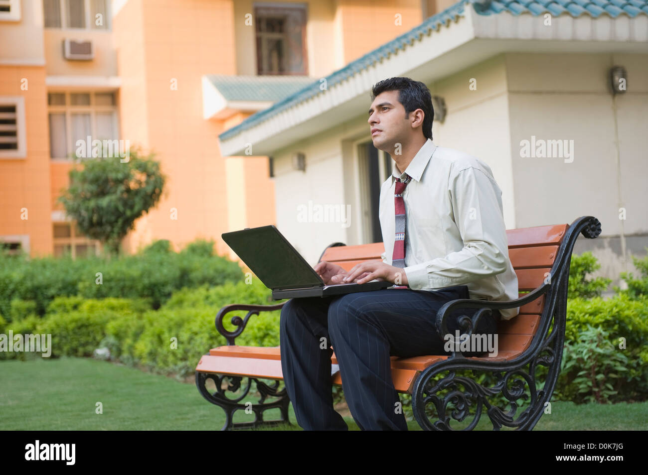 Businessman sitting on the bench and using a laptop Stock Photo - Alamy