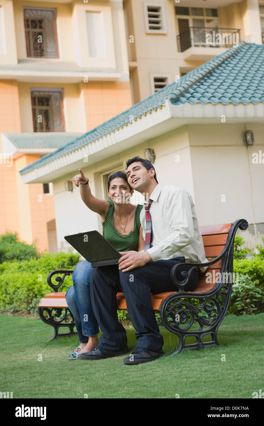 Couple sitting on the bench with laptop and pointing Stock Photo - Alamy