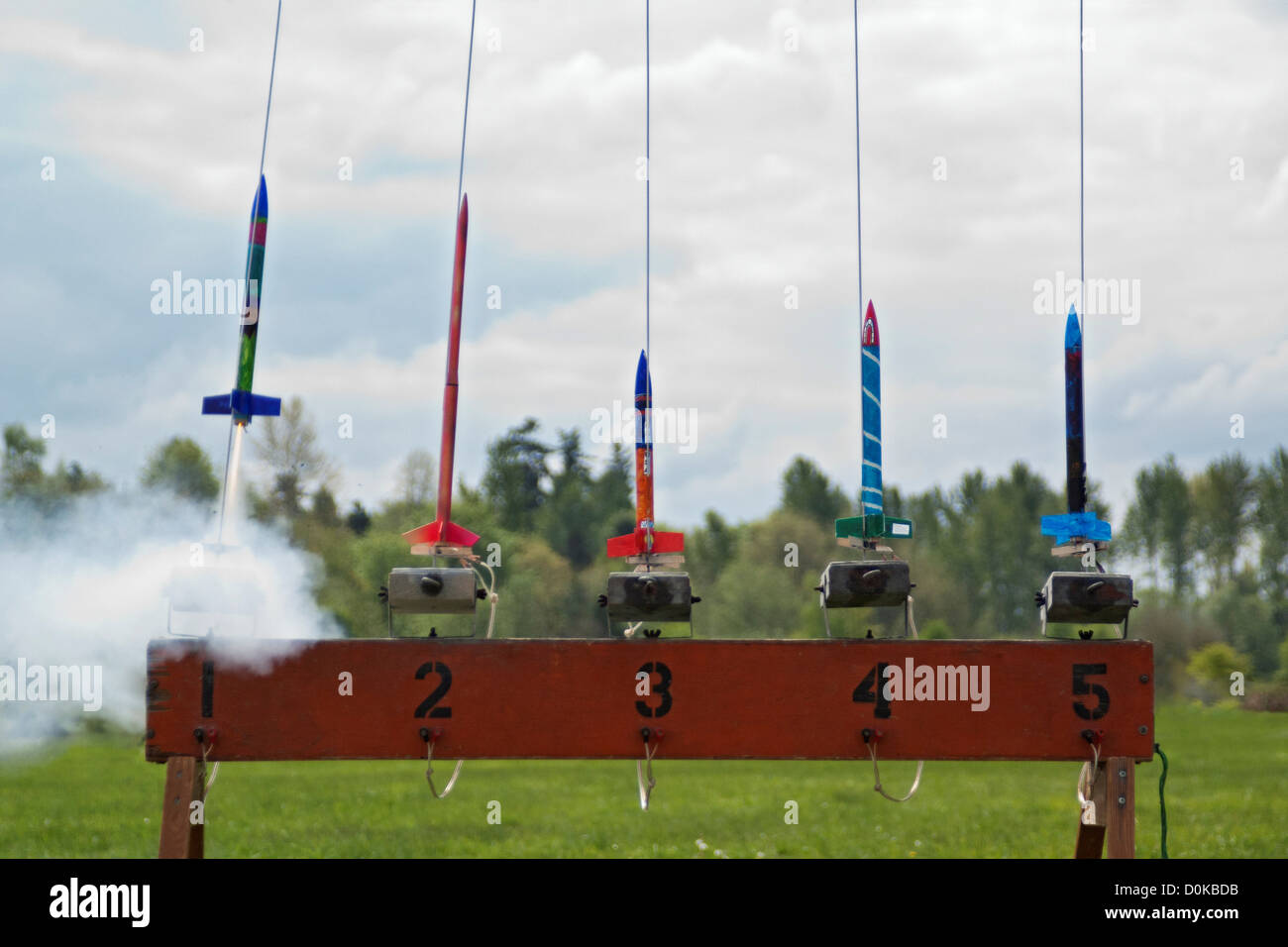 A row of brightly painted model rockets launch at a rocketry launch