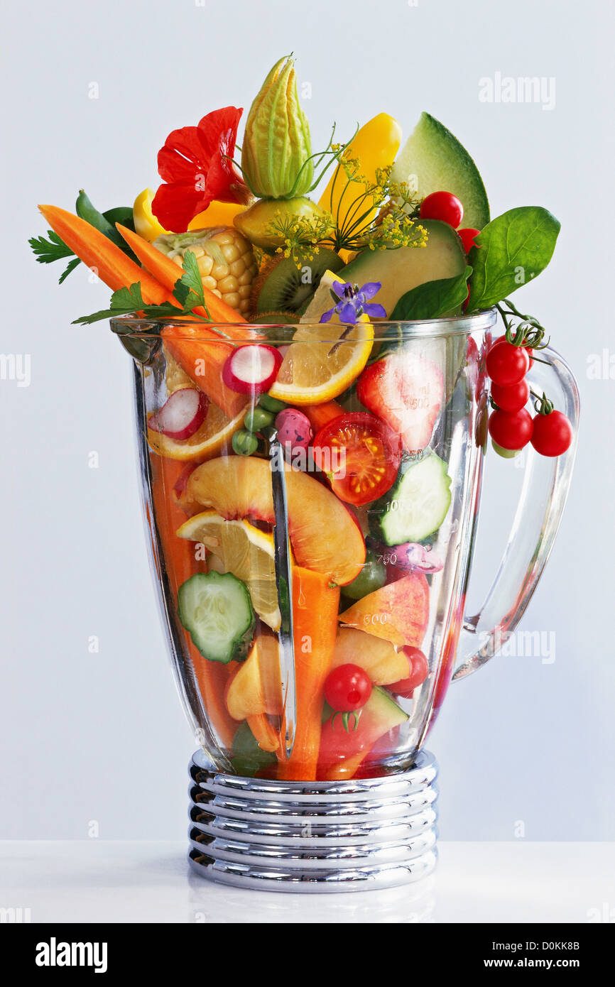 A collection of fruits, vegetables, and herbs and flowers in a blender