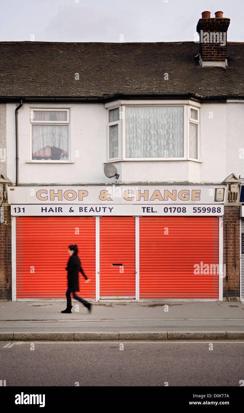 A woman walking past a closed beauty salon with red shutters in Rainham. Stock Photo