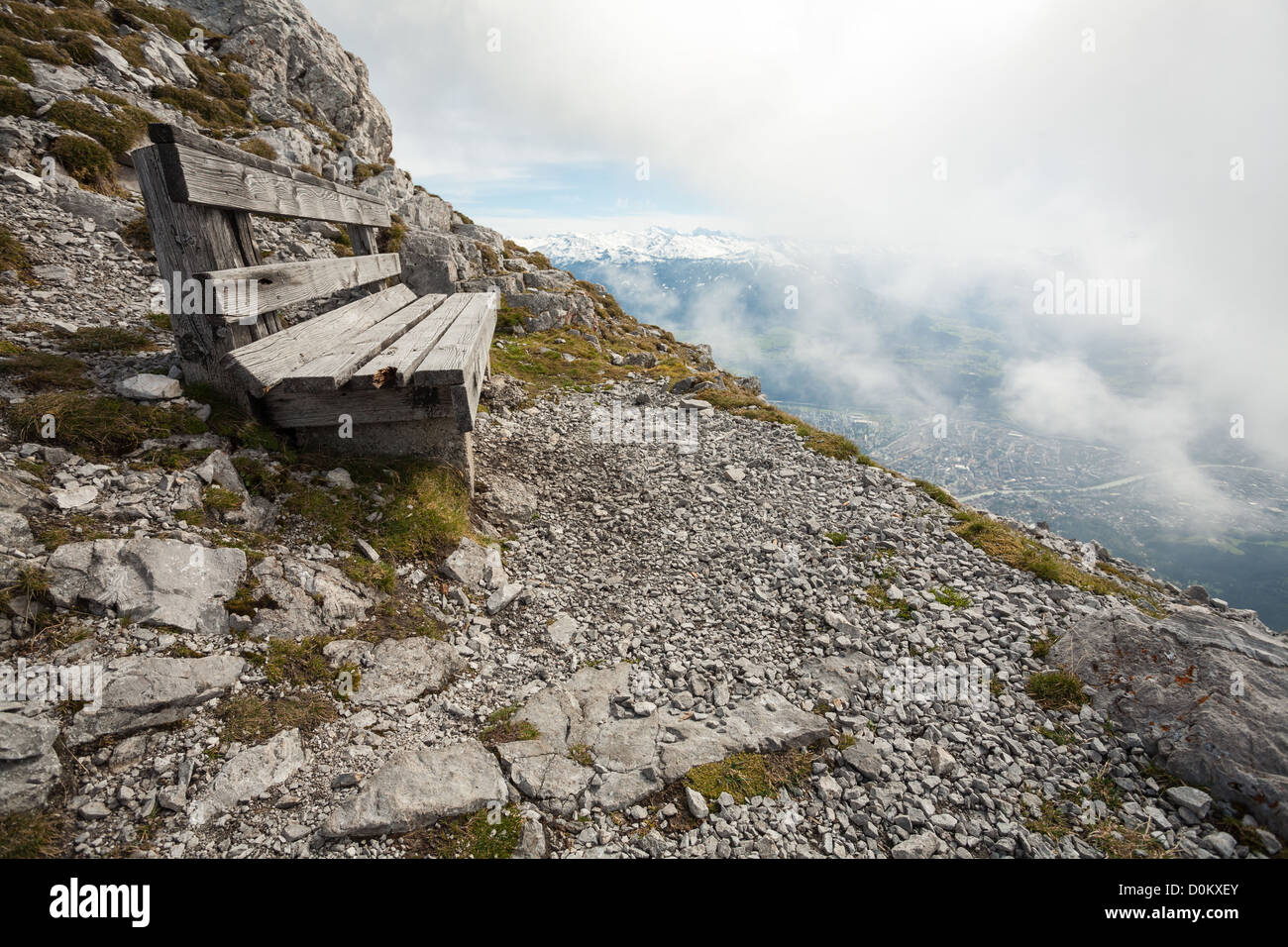 At bench seat on the edge of a rocky mountain overlooking Innsbruck which is beneath the clouds in the valley below. Stock Photo