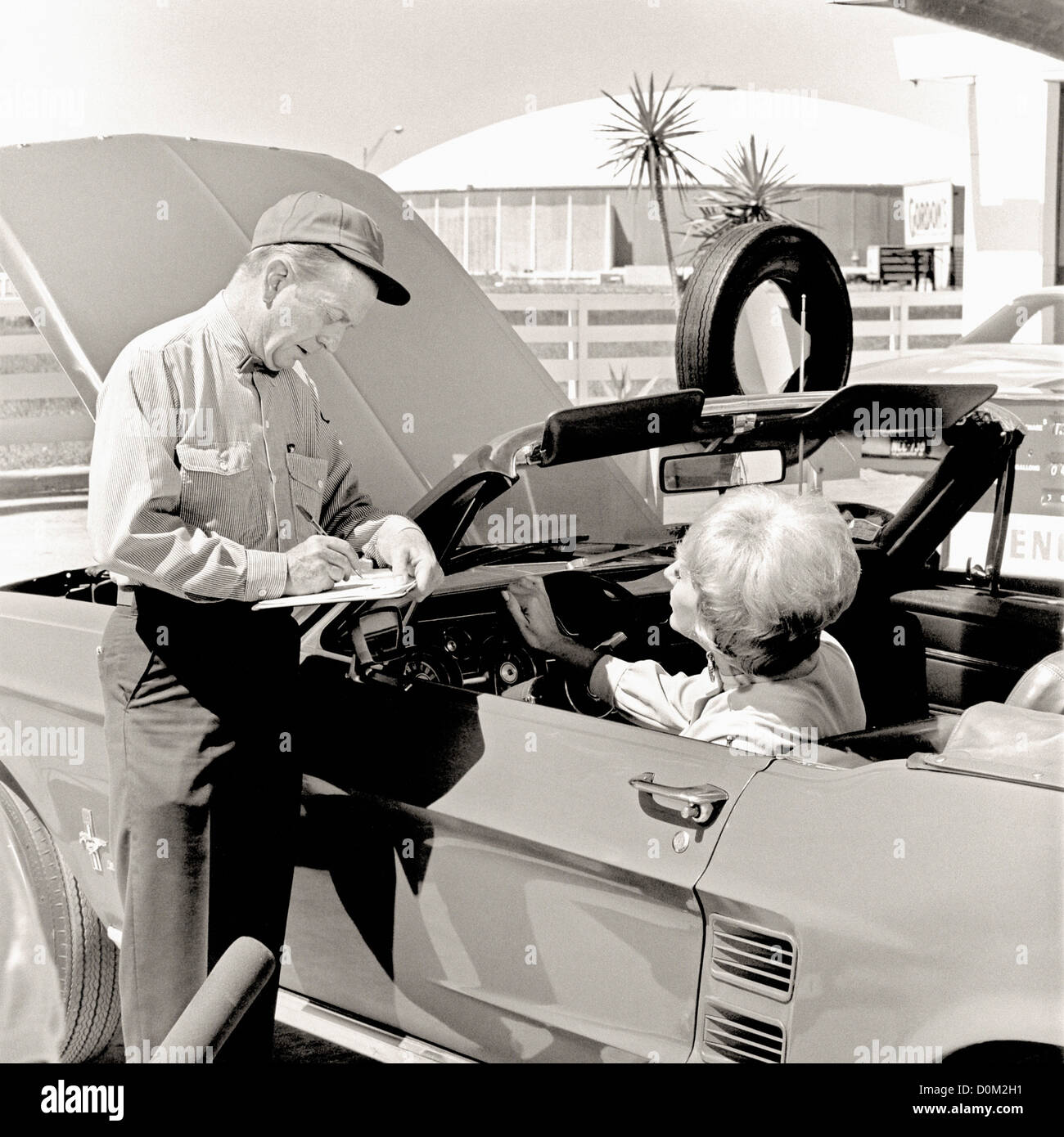 An ENCO service station attendant checks under hood Ford Mustang his customer.  Houston Astrodome is in background.  ENCO was Stock Photo