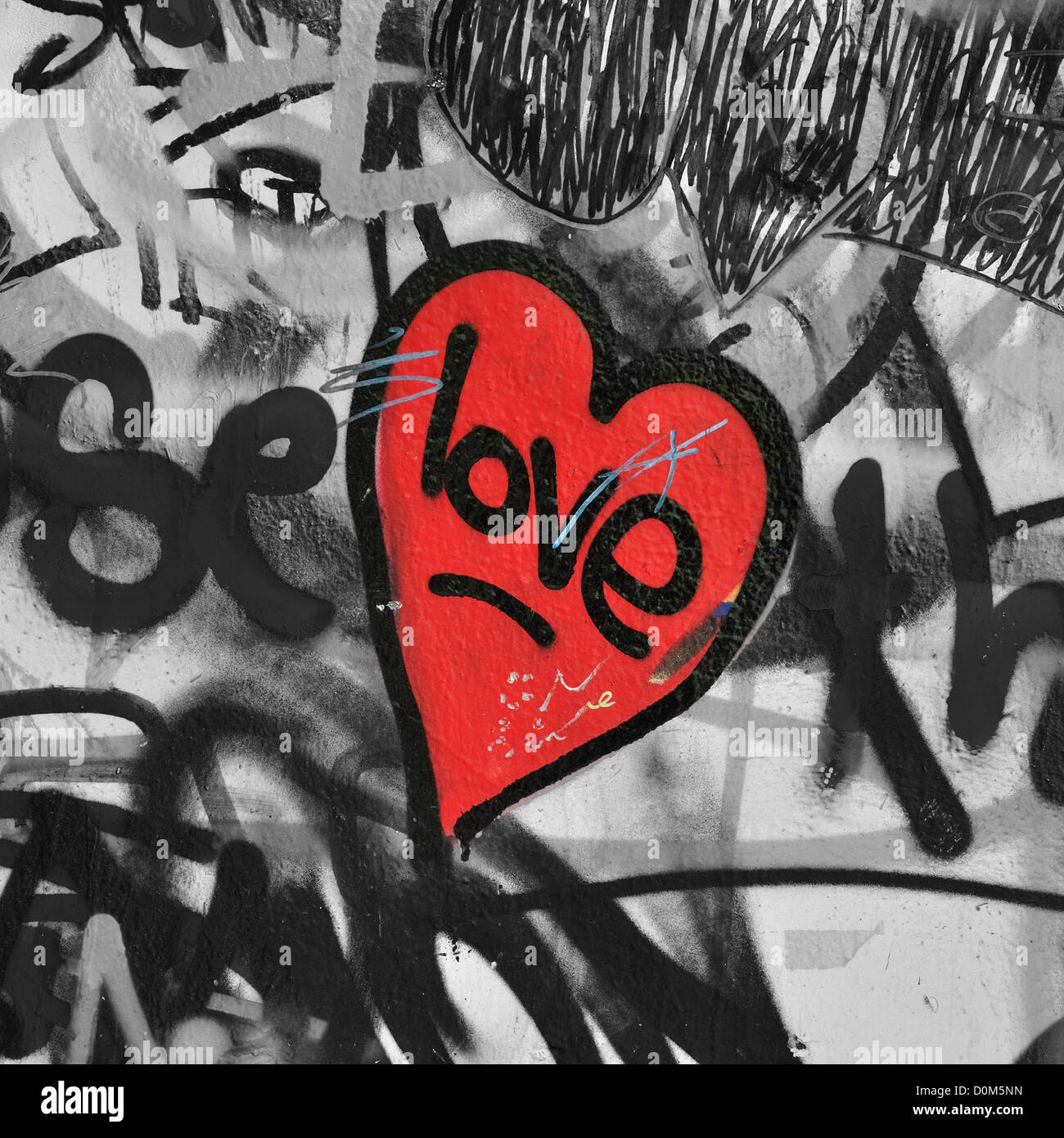 Red painted love heart on graffiti covered black and white wall background. Selective saturation. Stock Photo