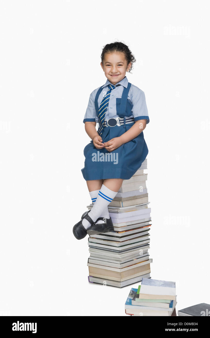 Schoolgirl sitting on a stack of books and smiling Stock Photo - Alamy