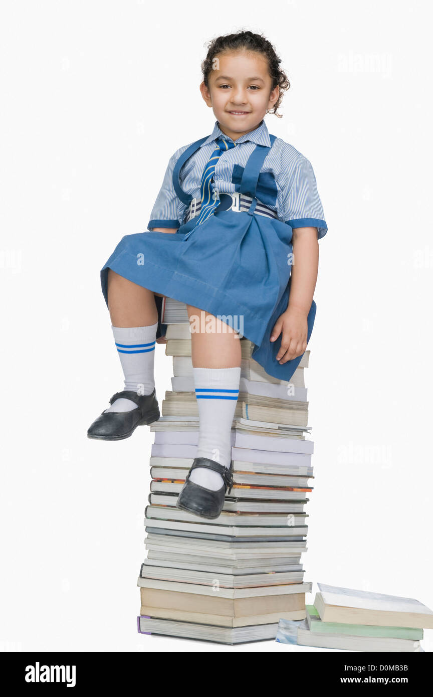 Schoolgirl sitting on a stack of books and smiling Stock Photo - Alamy