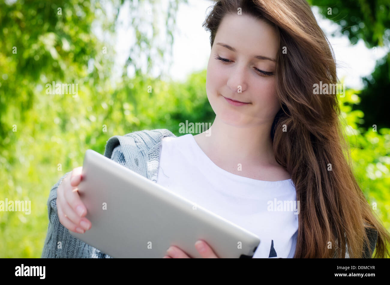Low angle view of an attractive casual young woman working on a touch screen tablet in the park Stock Photo