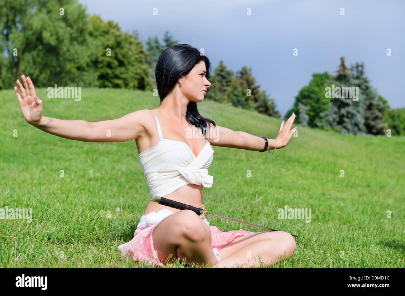 Beautiful woman meditates on green lawn with katana sword put on feet Stock Photo
