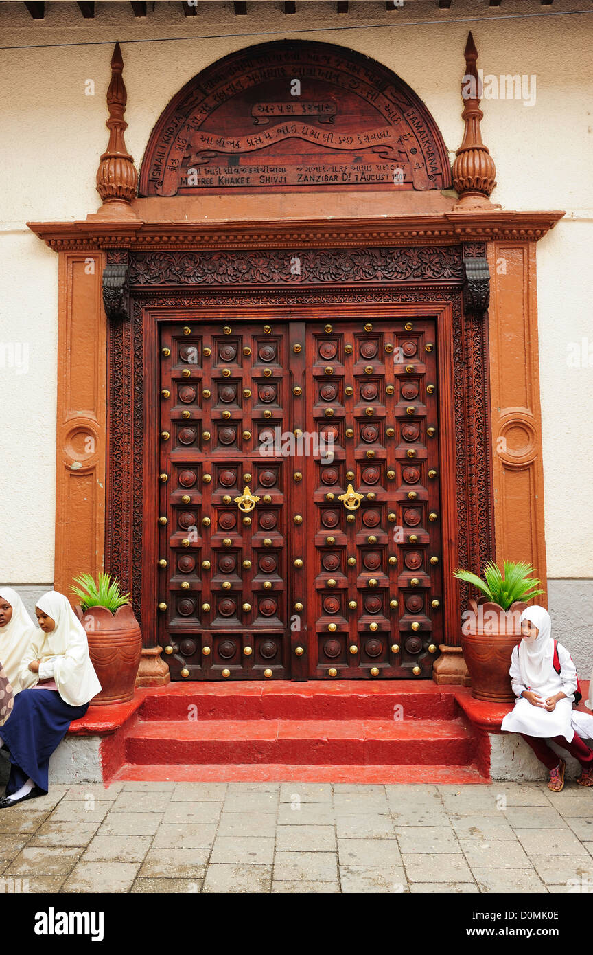 Young Muslim girls in front of carved wooden door in Stone Town, Zanzibar, Tanzania, East Africa Stock Photo
