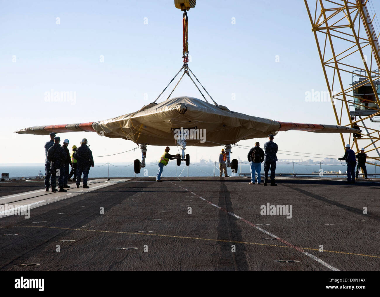 U.S. Navy Sailors assist with the onload of the X-47B Unmanned Combat Air System (UCAS) demonstrator aboard the aircraft carrier USS Harry S. Truman (CVN 75). The air vehicle arrived by barge from Naval Air Station Patuxent River, Md. Truman is the first Stock Photo