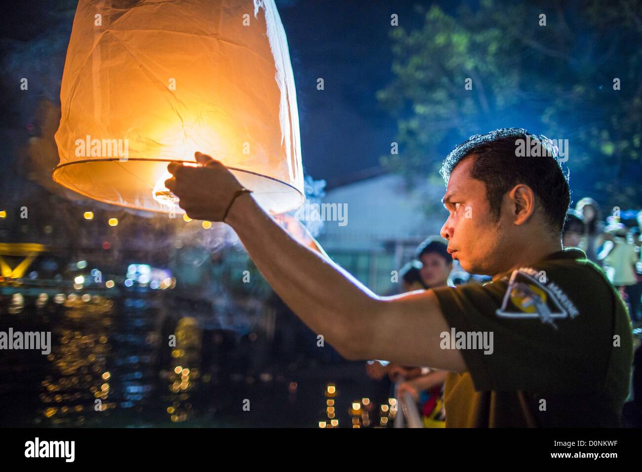 Nov. 28, 2012 - Bangkok, Thailand - A man tries to light a Khom Loi lantern  during Loy Krathong at Wat Yannawa in Bangkok. The lanterns are a part of the Loy Krathong tradition in northern Thailand, and are becoming popular in Bangkok. But authorities don't allow their use in Bangkok because of the fire danger. They try to stop people from launching the lanterns in Bangkok. Loy Krathong takes place on the evening of the full moon of the 12th month in the traditional Thai lunar calendar. In the western calendar this usually falls in November. Loy means 'to float', while krathong refers to the  Stock Photo