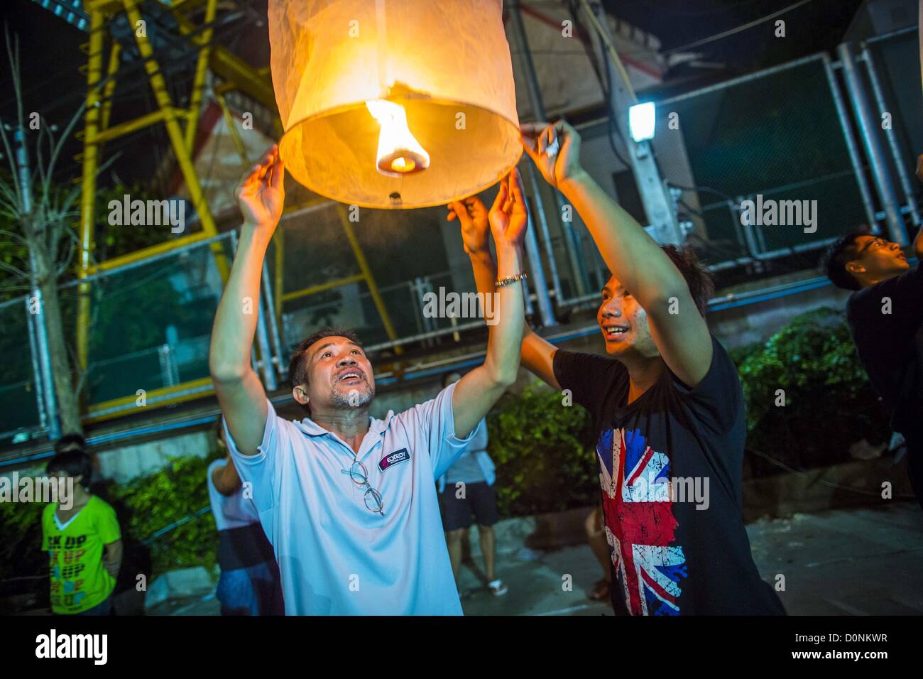 Nov. 28, 2012 - Bangkok, Thailand - People try to light a Khom Loi lantern  during Loy Krathong at Wat Yannawa in Bangkok. The lanterns are a part of the Loy Krathong tradition in northern Thailand, and are becoming popular in Bangkok. But authorities don't allow their use in Bangkok because of the fire danger. They try to stop people from launching the lanterns in Bangkok. Loy Krathong takes place on the evening of the full moon of the 12th month in the traditional Thai lunar calendar. In the western calendar this usually falls in November. Loy means 'to float', while krathong refers to the u Stock Photo