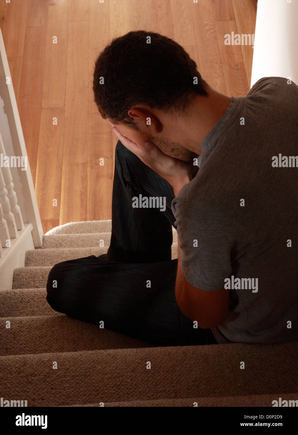 Young man sitting on the stairs, his hand covering his face. Rear view. expressing negativity Stock Photo