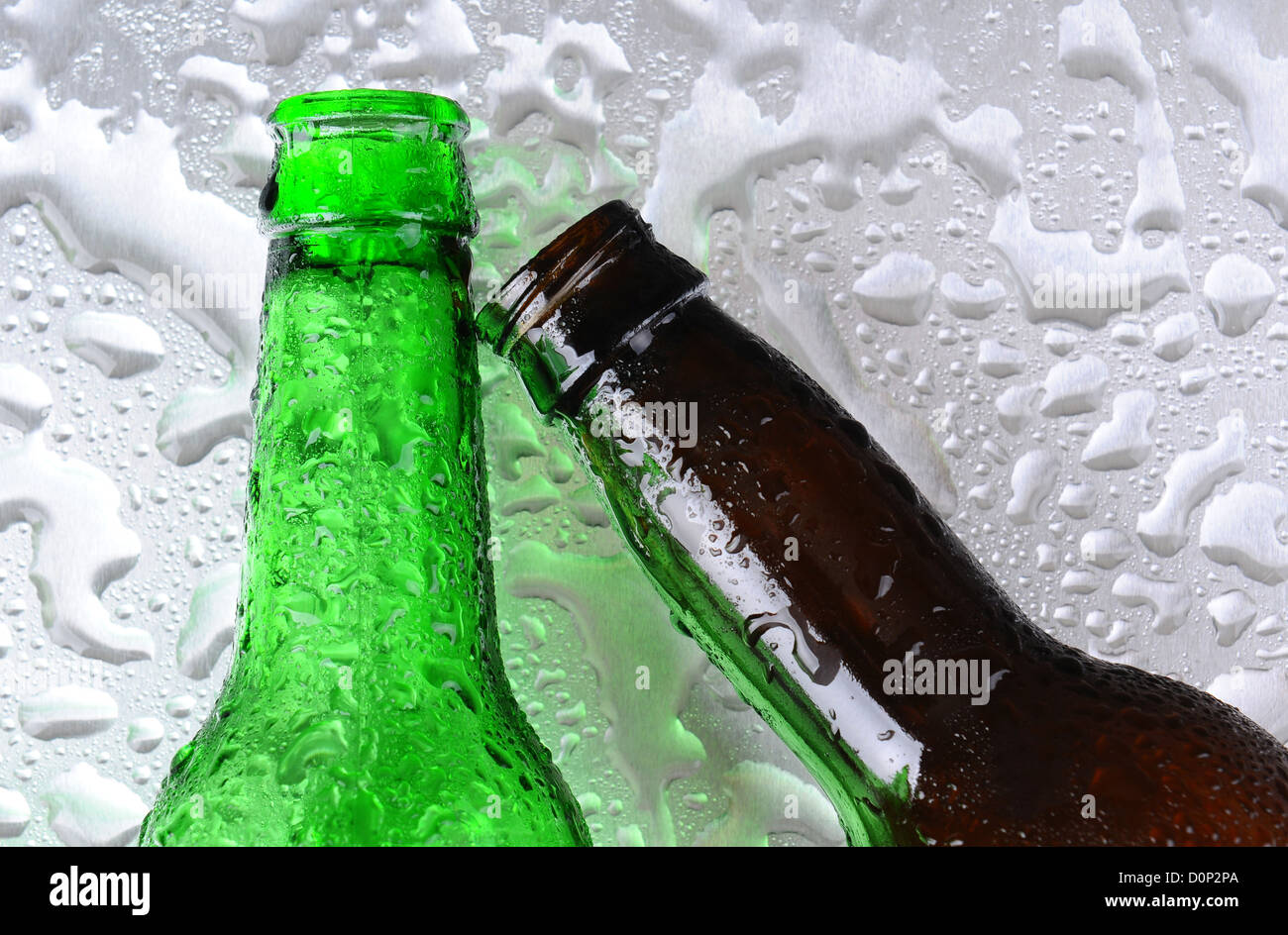 Closeup of two beer bottles on a wet stainless steel surface. One bottle is green the other brown. Stock Photo