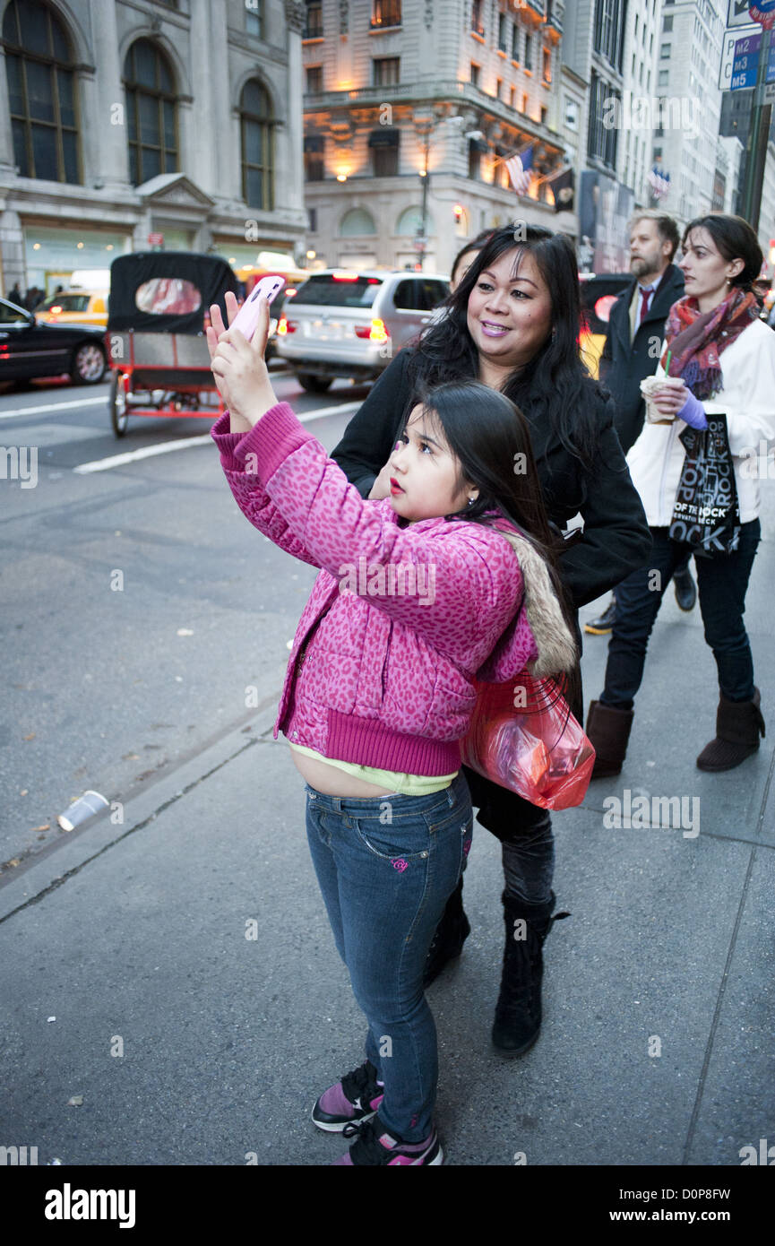 Hispanic girl wearing lipstick takes a photograph on Fifth Avenue in Manhattan during the Thanksgiving holiday weekend, 2012. Stock Photo