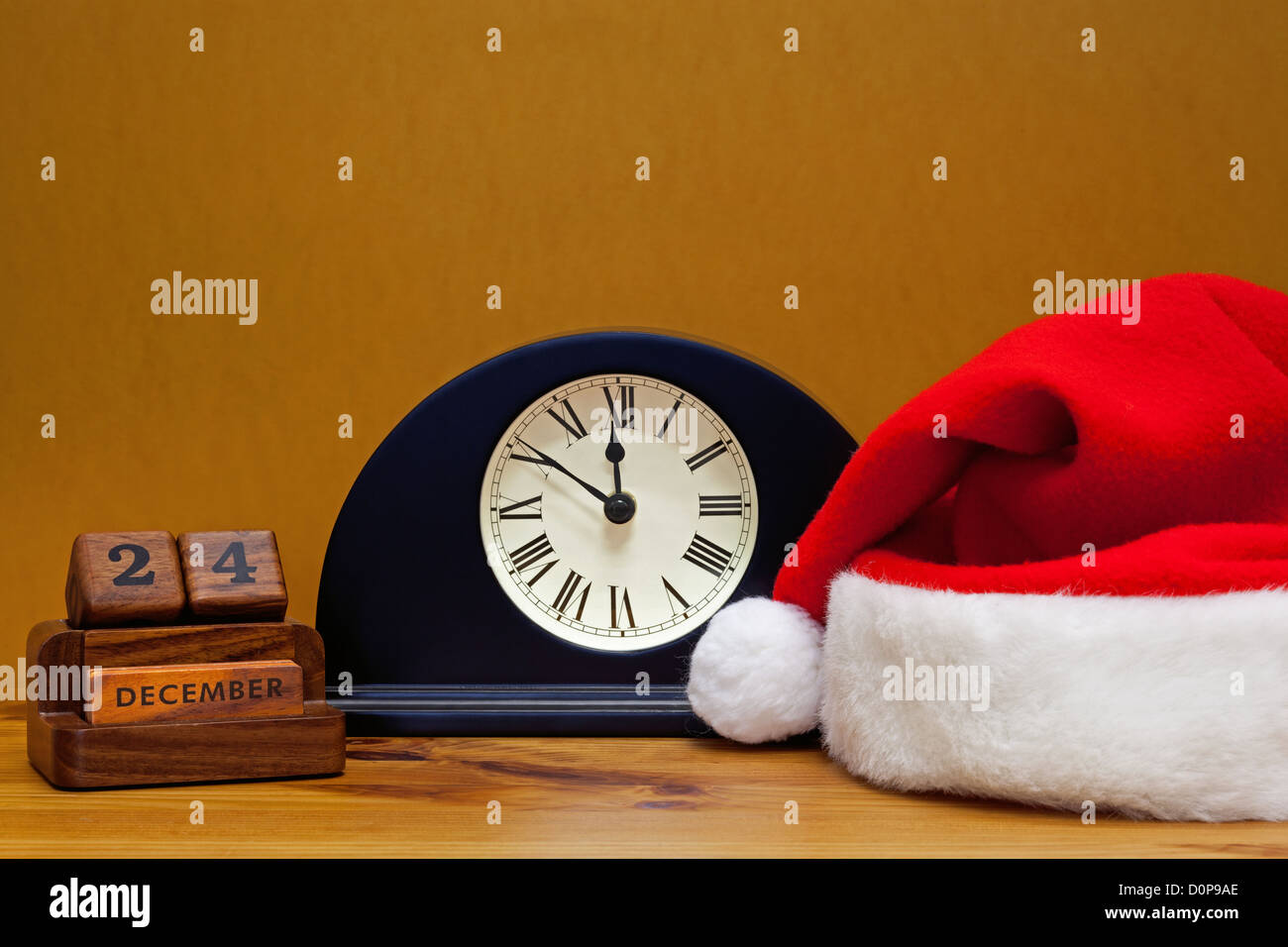 A hall table clock shows it's close to midnight on Christmas Eve, with desk calendar and Santa Claus hat. Stock Photo