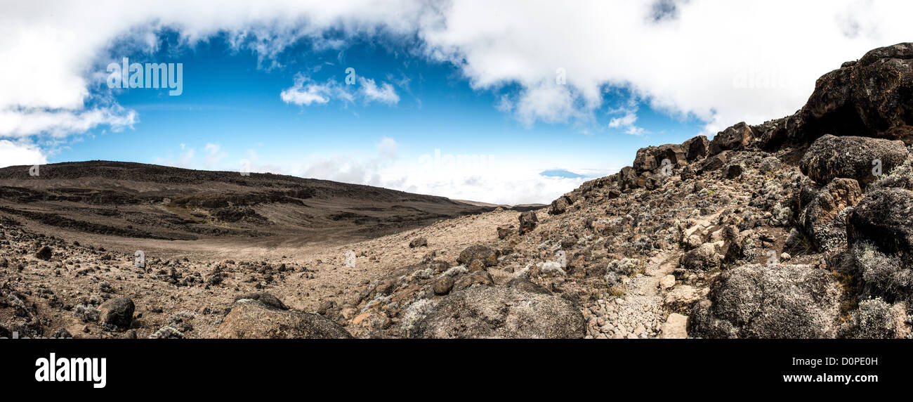 MT KILIMANJARO, Tanzania - A panorama of the rocky, rugged apline desert on Mt Kilimanjaro Lemosho Route. These shots were taken on the trail between Moir Hut Camp and Lava Tower at approximately 14,500 feet. In the far distance is the summit of Mt Meru peaking up through the clouds. Stock Photo