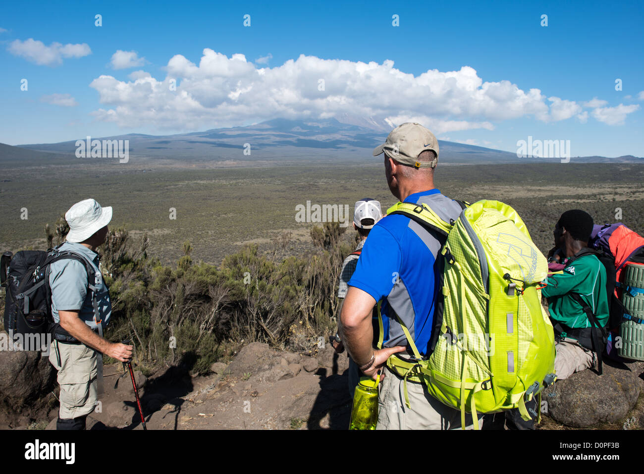 MT KILIMANJARO, Tanzania - Hikers in the heath zone on Mt Kilimanjaro's Lemosho Trail with the peak of the mountain far in the distance partly obscured by clouds. Stock Photo