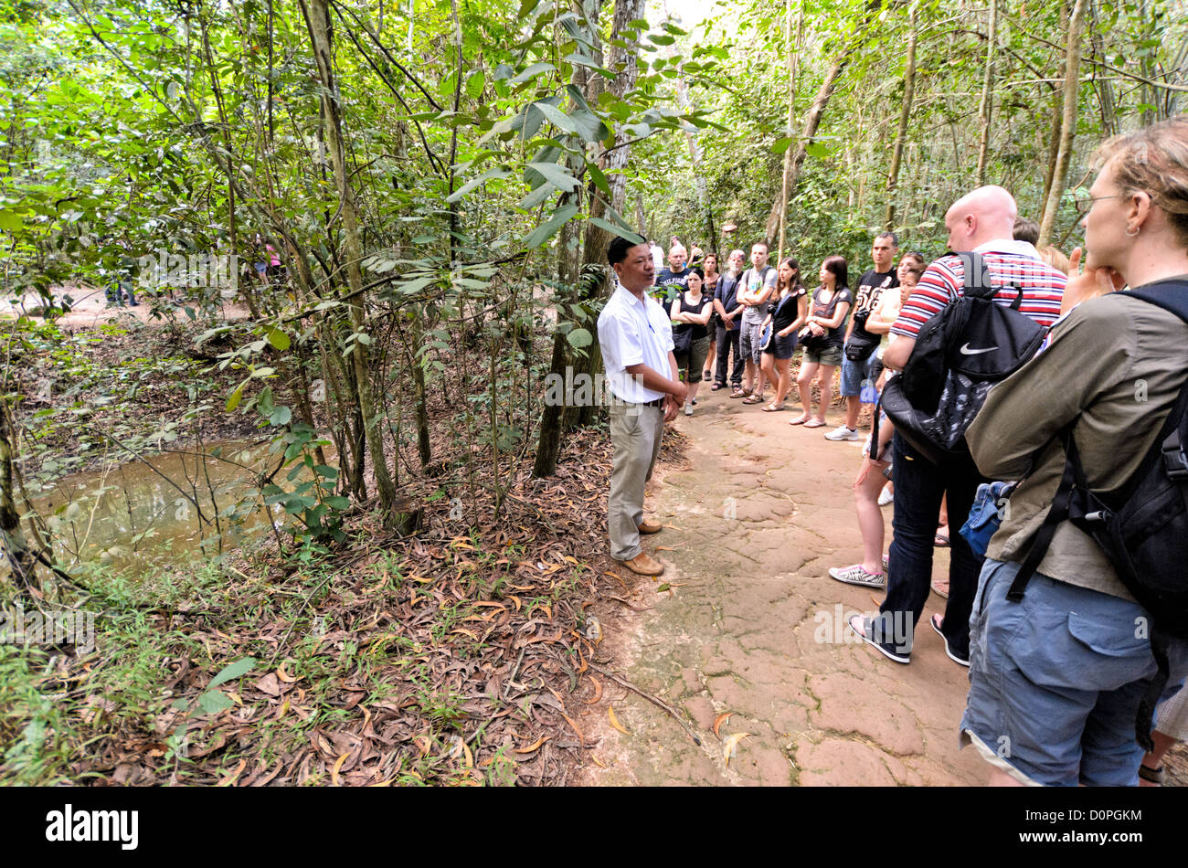 HO CHI MINH CITY, Vietnam - A tour guide explains to tourist what the American bombing campaign did to the surrounding landscape. At left of the frame is one of the many bomb craters that pockmark the area. The Cu Chi tunnels, northwest of Ho Chi Minh City, were part of a much larger underground tunnel network used by the Viet Cong in the Vietnam War. Part of the original tunnel system has been preserved as a tourist attraction where visitors can go down into the narrow tunnels and see exhibits on the defense precautions and daily life of the Vietnamese who lived and fought there. Stock Photo