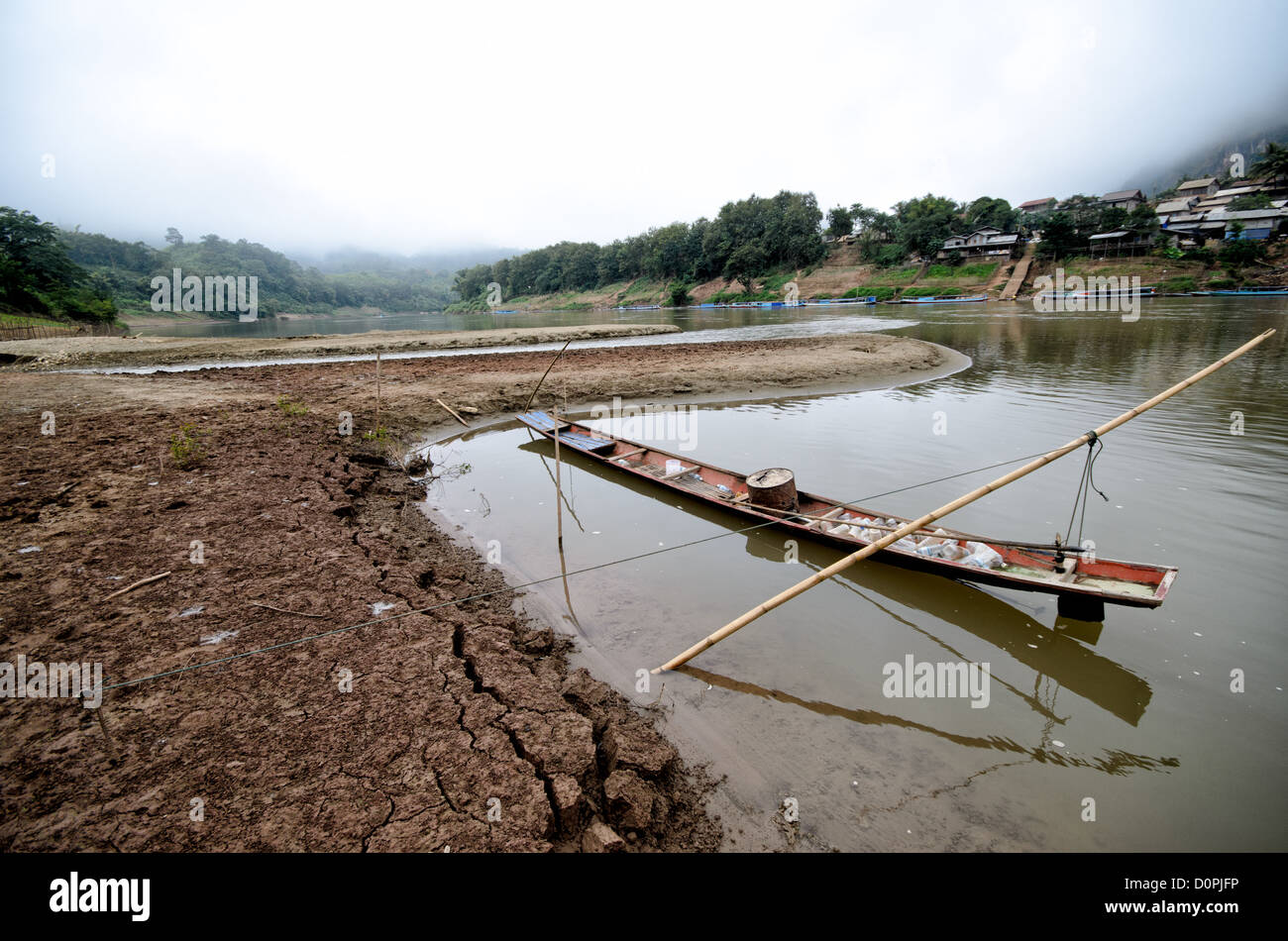 NONG KHIAW, Laos - A long, thin wooden boat is moored by bamboo poles in a small sandy bay along the sandy shores of the Nam Ou (River Ou) in Nong Khiaw in northern Laos. Stock Photo