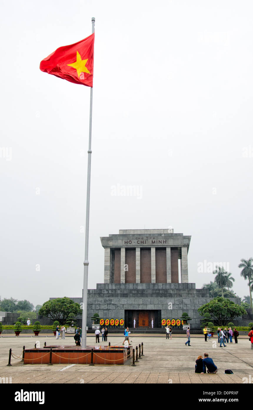 HANOI, Vietnam - A Vietnamese flag flies in front of the Ho Chi Minh Mausoleum as tourists wander in the square in front. A large memorial in downtown Hanoi surrounded by Ba Dinh Square, the Ho Chi Minh Mausoleum houses the embalmed body of former Vietnamese leader and founding president Ho Chi Minh. Stock Photo