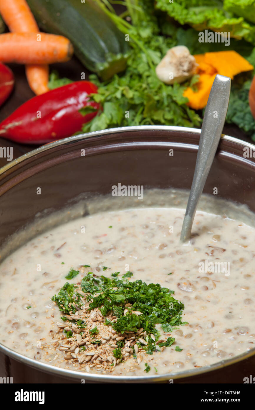 Chopped herbs and garlic being added to a large pot of creamy vegetable soup being prepared in the kitchen Stock Photo