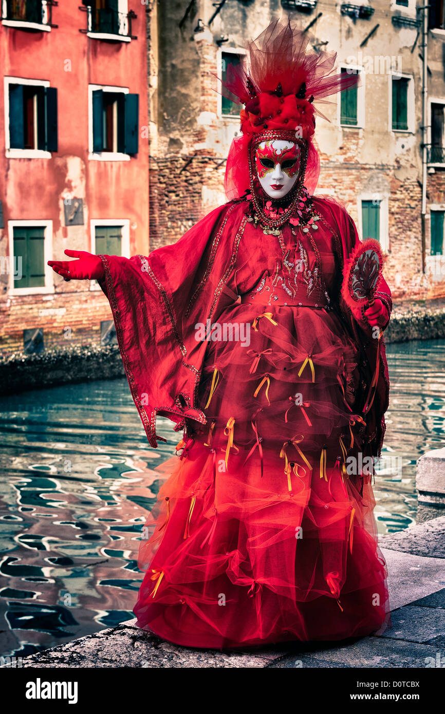 Masked participant posing along a canal on Burano Island during Carnival in Venice, Italy Stock Photo