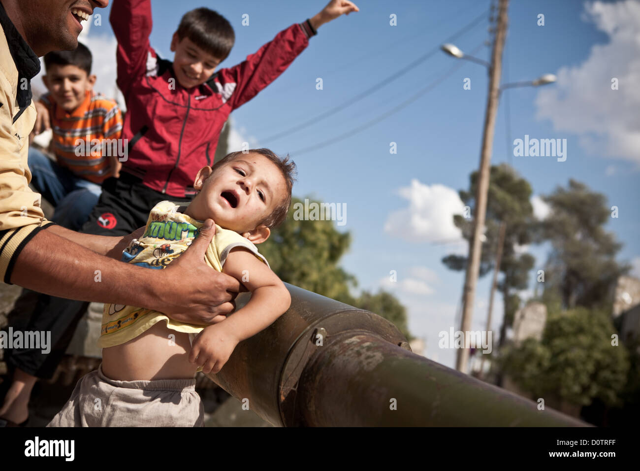 5/10/12, Azaz, Syria. A father holds his child up against the barrel of a disabled tank in the Syrian town of Azaz. Stock Photo