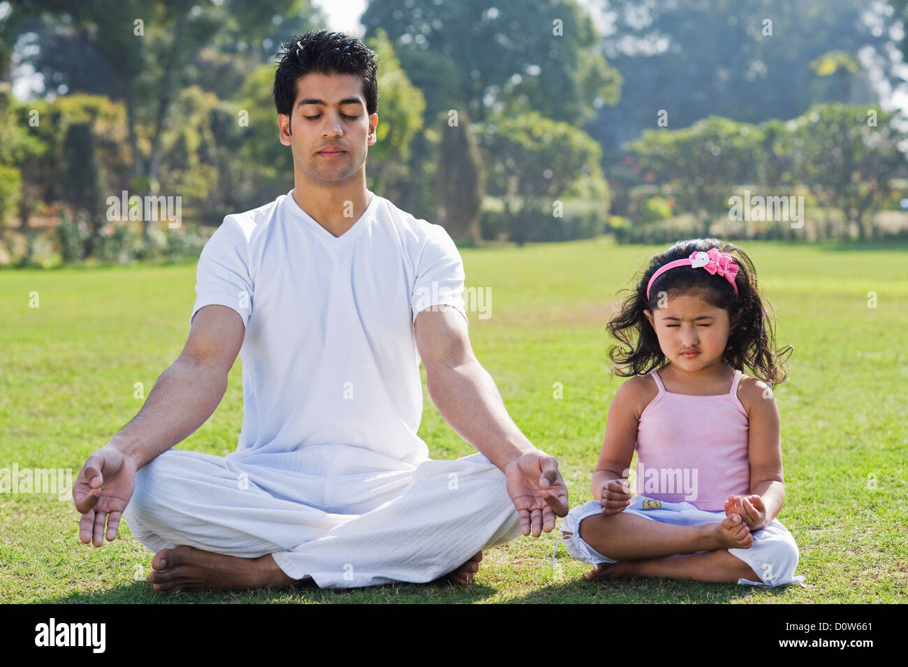 Man meditating with his daughter in lawn, Gurgaon, Haryana, India Stock Photo