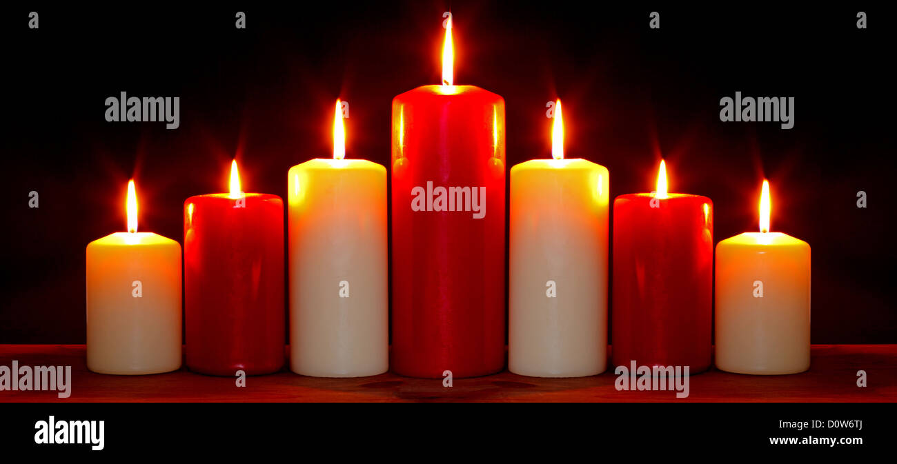 Still life photo of red and white church candles arranged in an arch burning with bright flames against a black background. Stock Photo
