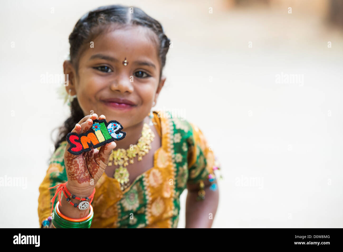 Smiling Indian girl holding a SMILE multicoloured embroidery patch. Andhra Pradesh, India Stock Photo