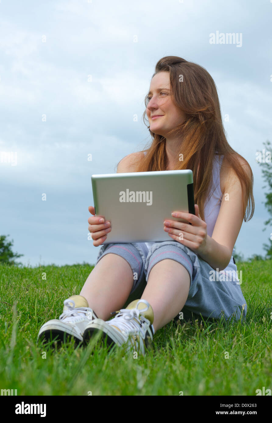 Low angle view of a happy laughing woman sitting on grass with a touchscreen tablet in her hands Stock Photo