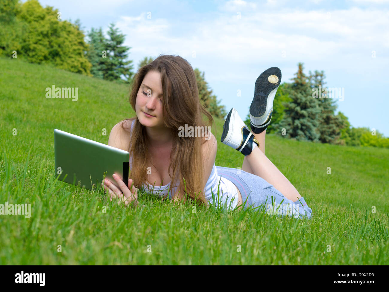 Woman lying on a grassy slope outdoors relaxing with a touchscreen tablet Stock Photo