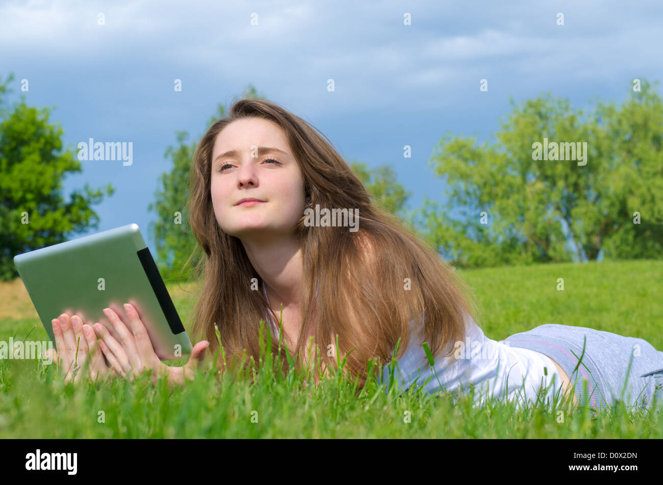 Attractive young woman lying on the grass with her touchscreen tablet daydreaming in the sunshine Stock Photo