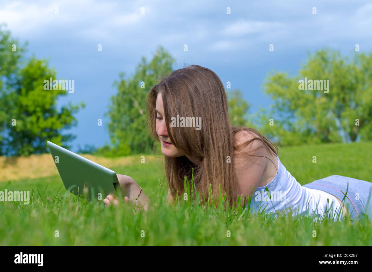 Closeup of a young woman working on her tablet lying in the sunshine on green grass Stock Photo