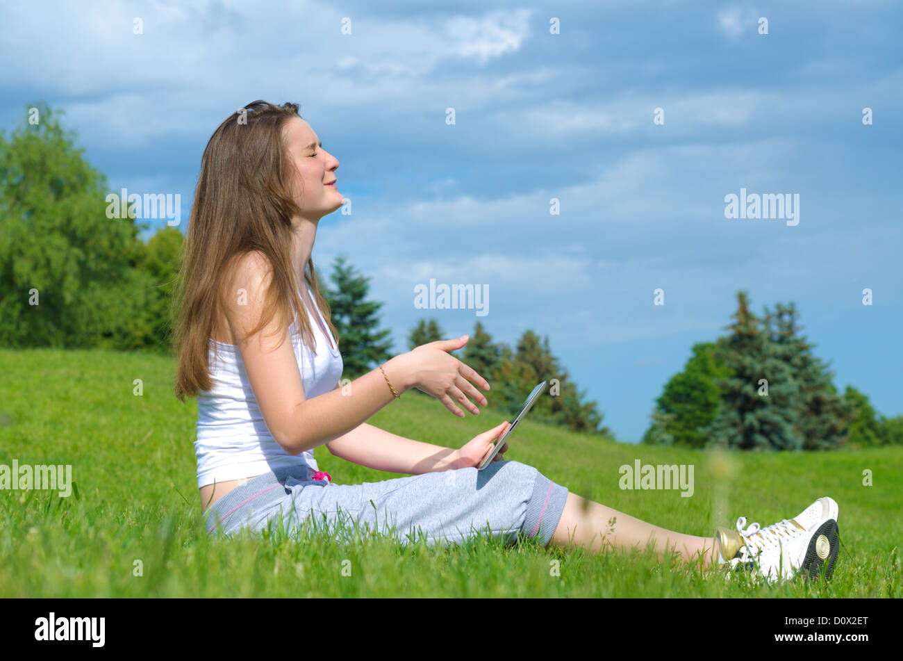 Young girl memorising something on her tablet with her eyes closed as she studies for her classes in the park Stock Photo