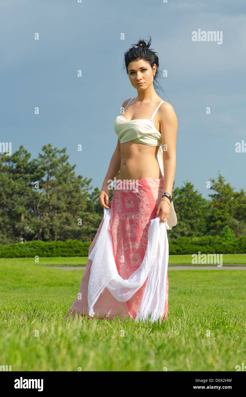 Glamorous woman in a long skirt and bare belly trailing a scarf in her hands posing in a park Stock Photo