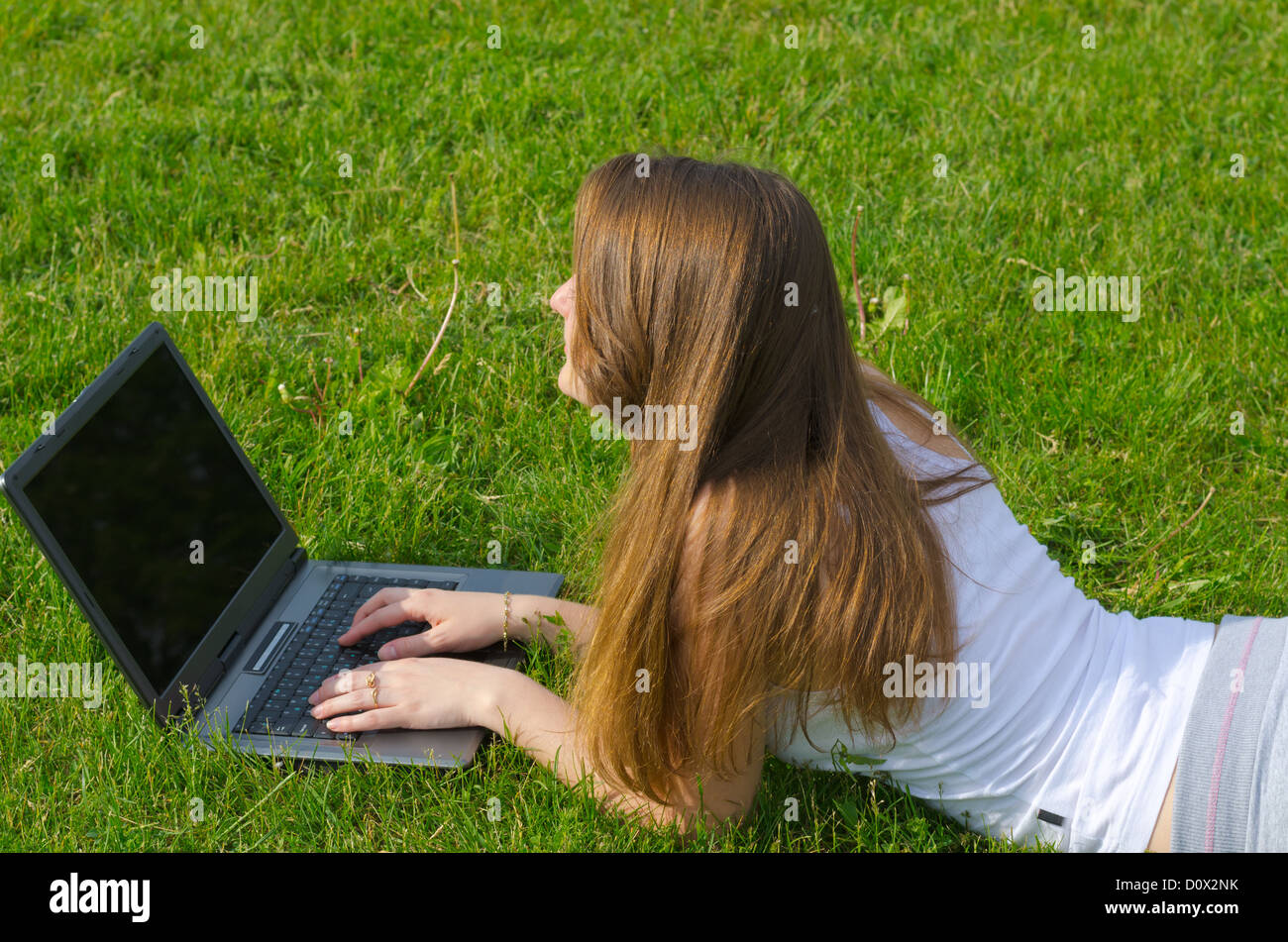 High angle view of a young woman with long brunette hair lying on the grass working on her laptop Stock Photo