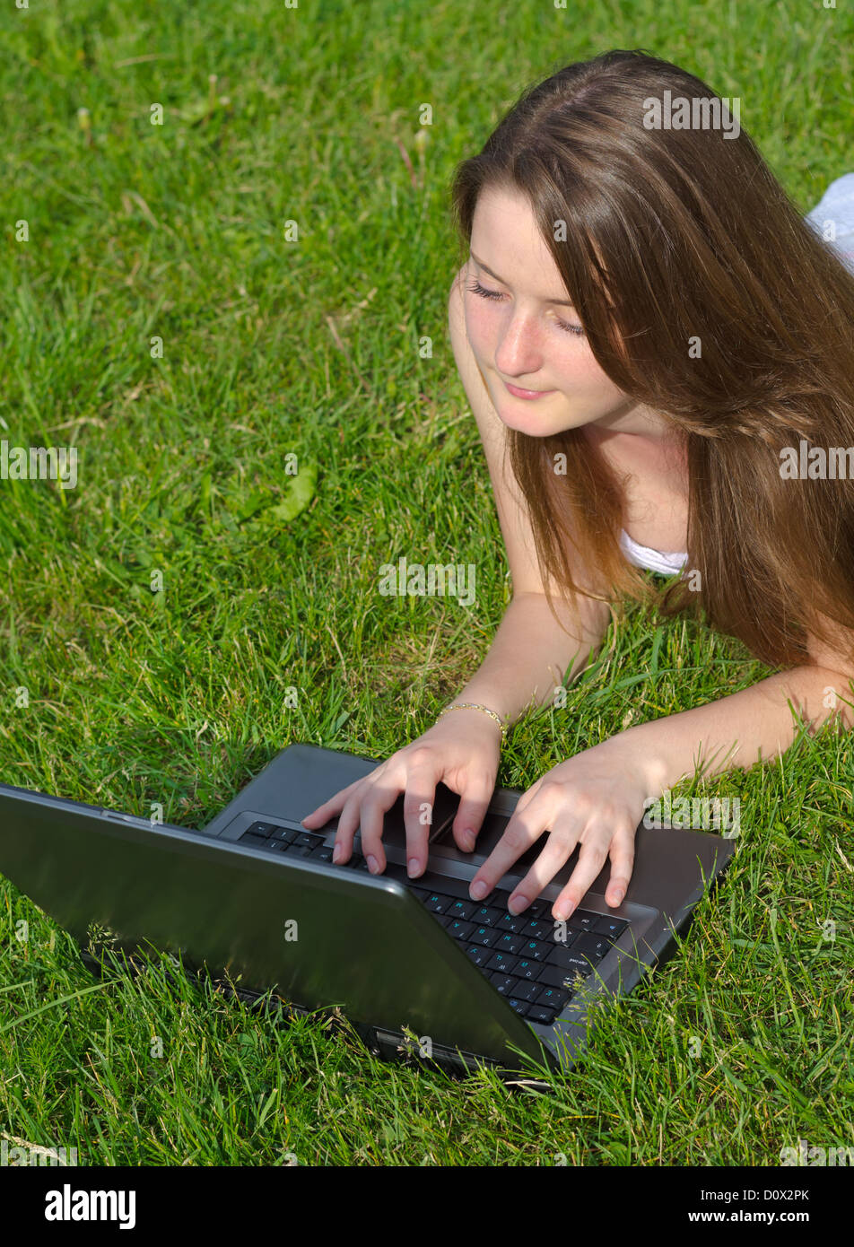 High angle view of an attractive young woman using a laptop while lying on her stomach in green grass Stock Photo