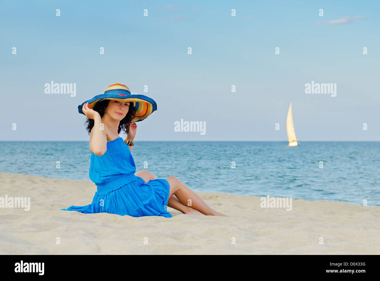 Attractive woman in blue dress sitting by the sea on beautiful sandy beach Stock Photo